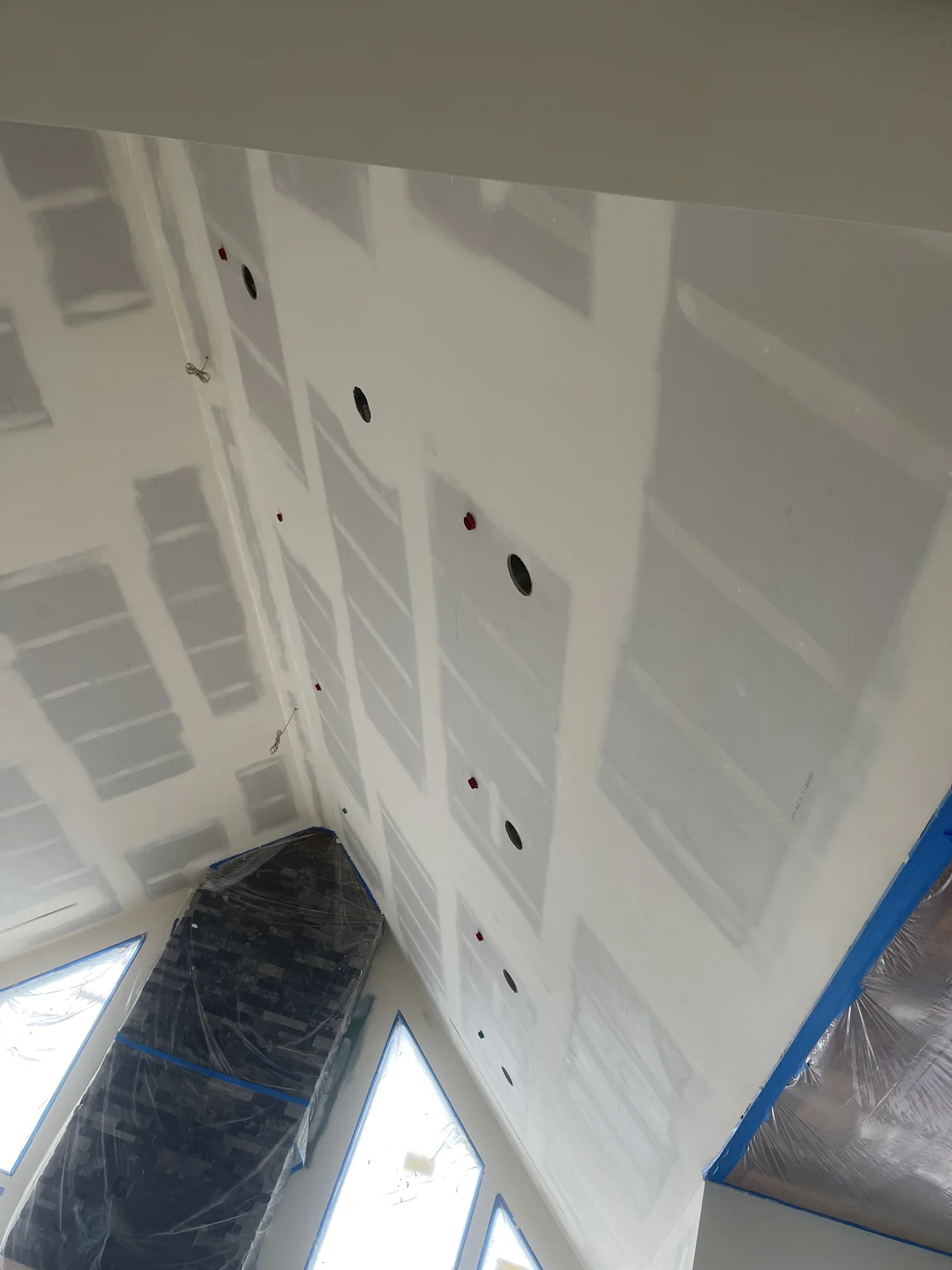 Taped drywall seams following an angled ceiling above tall windows.
