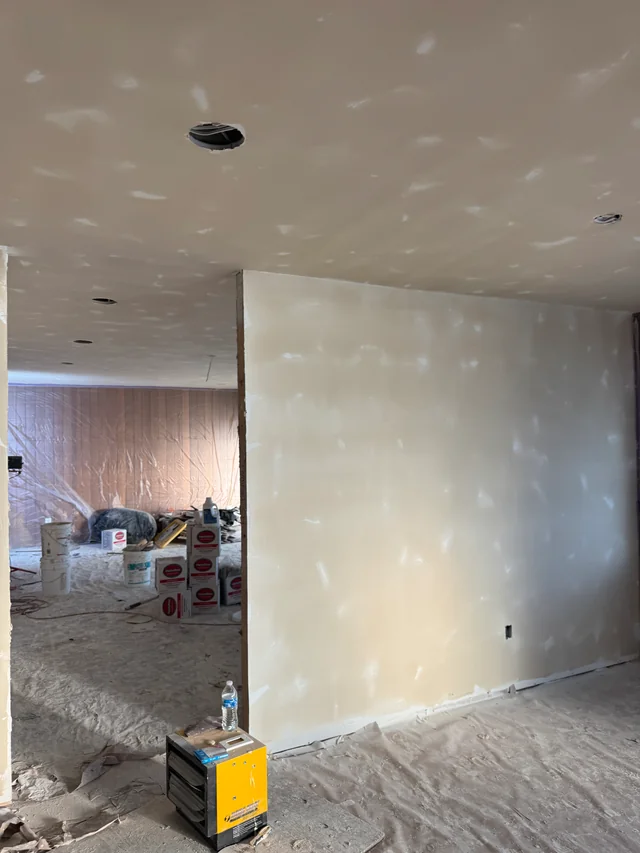 Joint compound on drywall walls and ceiling around a newly finished partition, with the floor protected below.