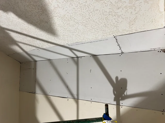 New drywall patches secured along the upper stairwell wall beside the existing textured ceiling.