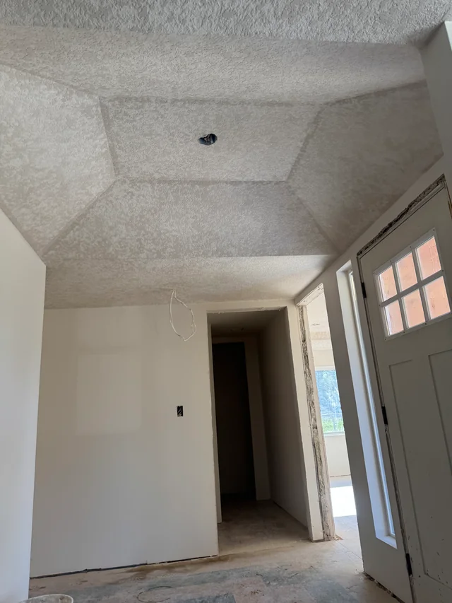 A textured tray ceiling above smooth walls, a doorway and an entry door.