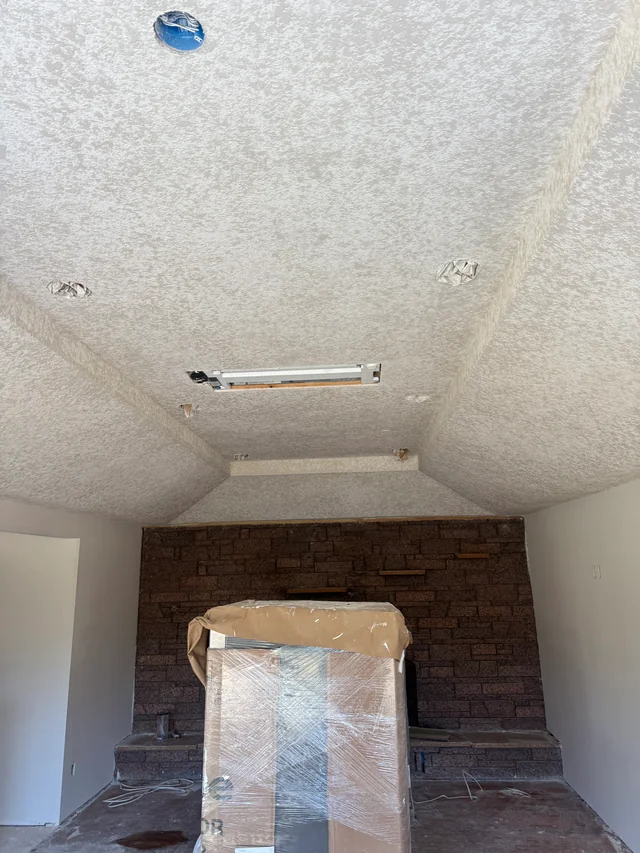 A textured ceiling with recessed light openings above a living room with a brick fireplace and protected fixtures.
