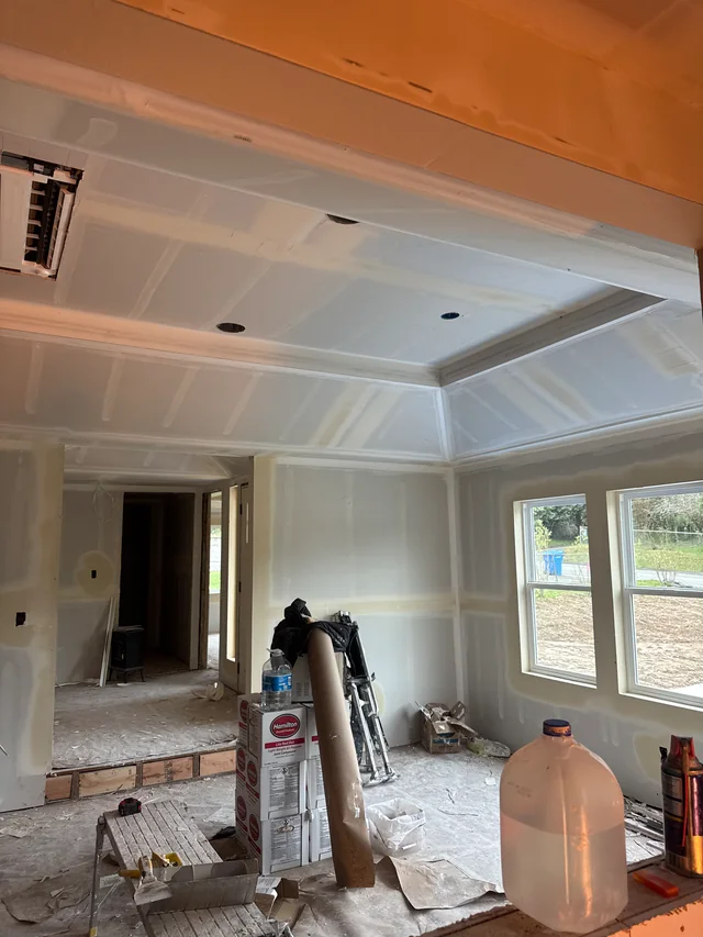Drywall joints taped across a stepped tray ceiling and room walls, with materials and floor protection in place.