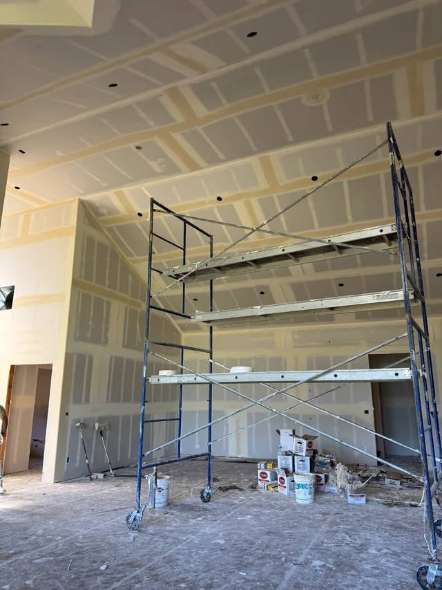 Taped drywall on tall walls and a vaulted ceiling, with scaffolding set up beneath the ceiling.