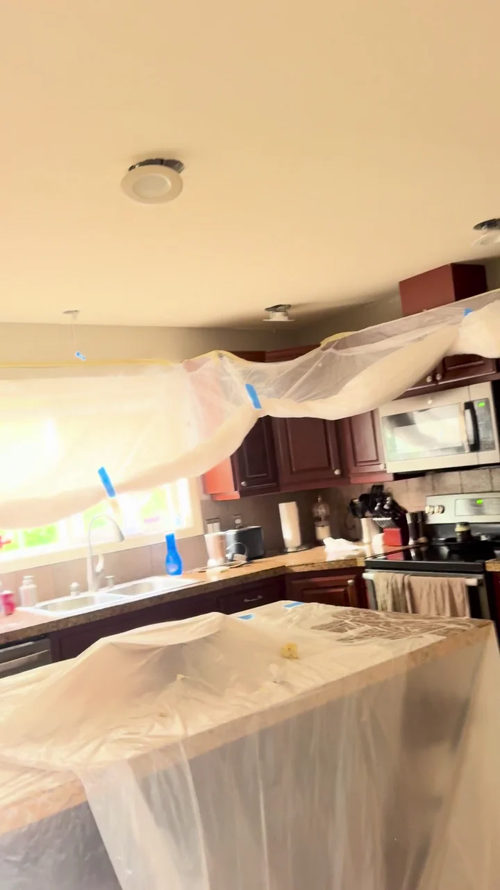 A kitchen and living area with cabinets, furniture and fixtures covered beneath the ceiling work.