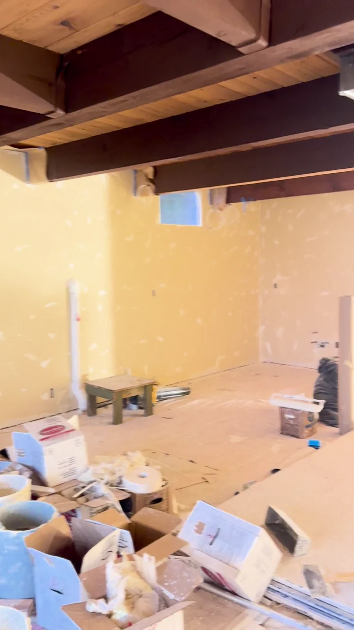 Drywall seams and fasteners being finished around exposed ceiling beams and interior doorways.
