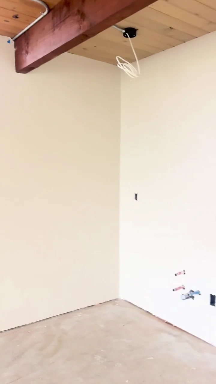 Smooth wall surfaces beneath exposed wood beams, with floors protected as work continues.