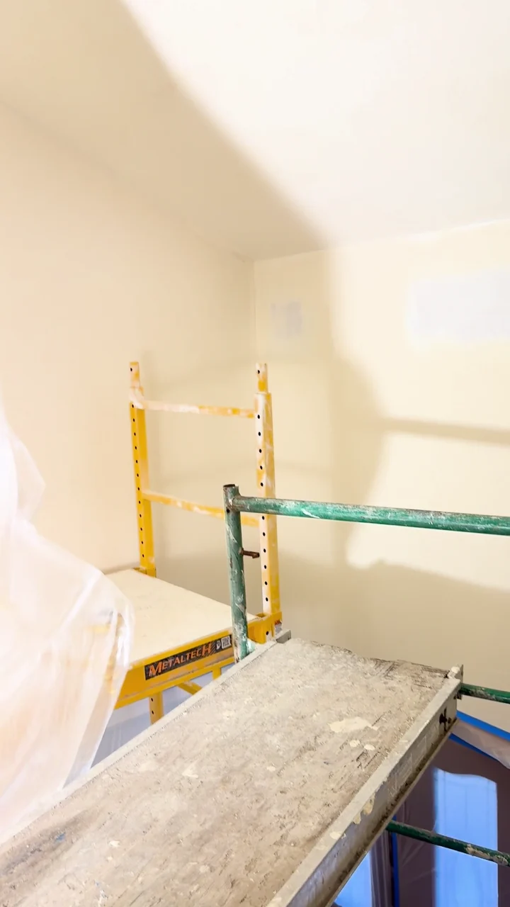 Tall stairwell walls during finishing, with scaffolding, tools and protective sheeting in place.