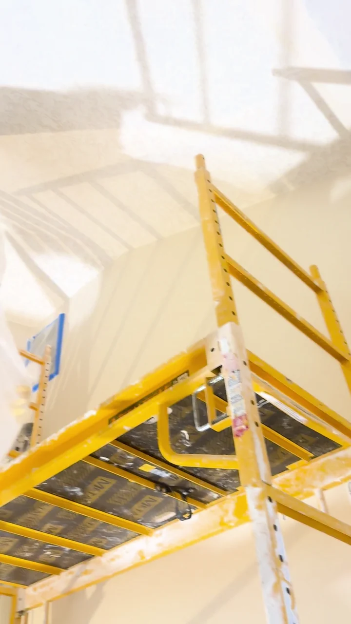 Scaffolding and protective sheeting set up around high stairwell walls.