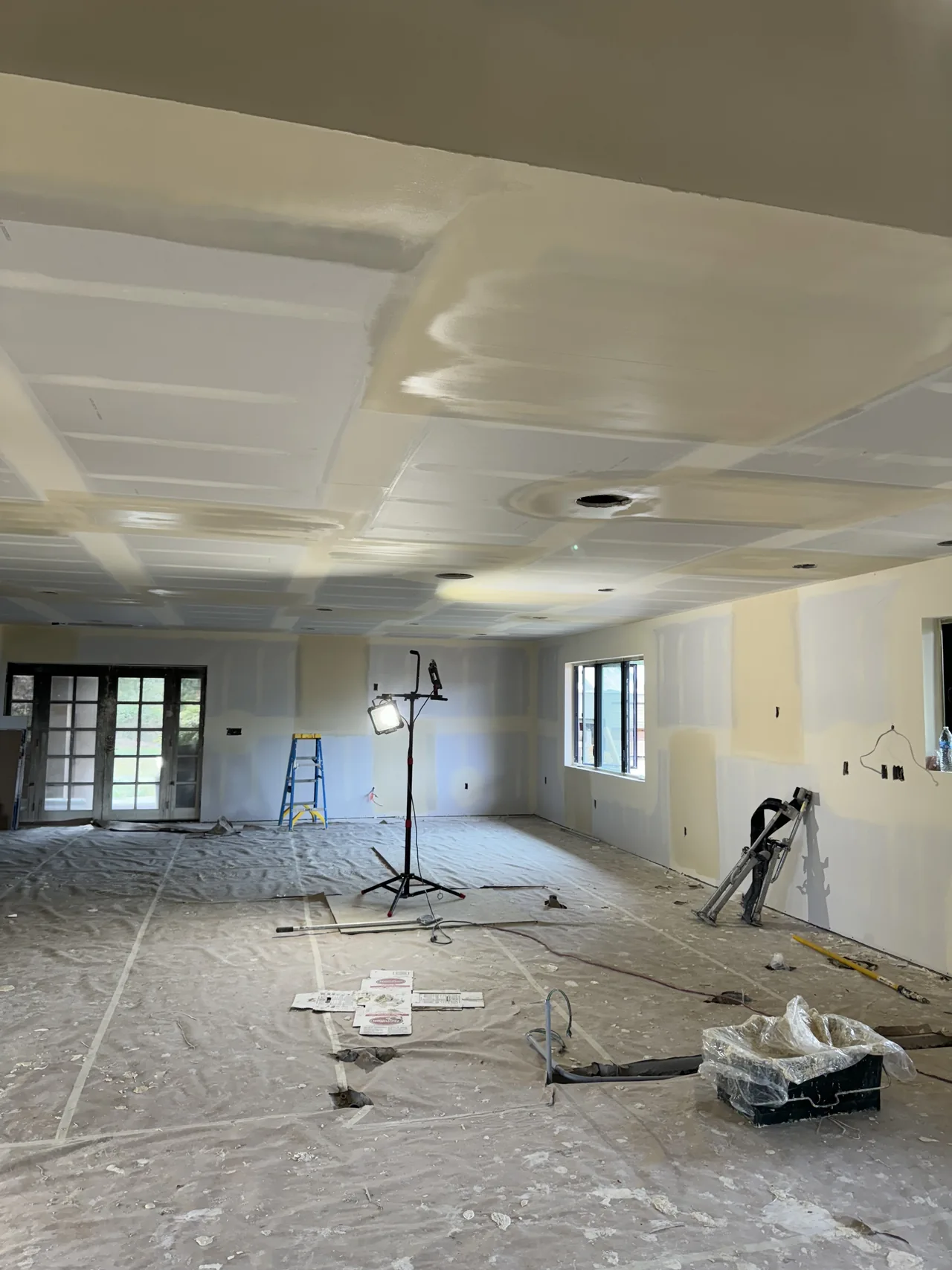 Drywall taping across walls and ceiling seams in a wide room during an Altus project.