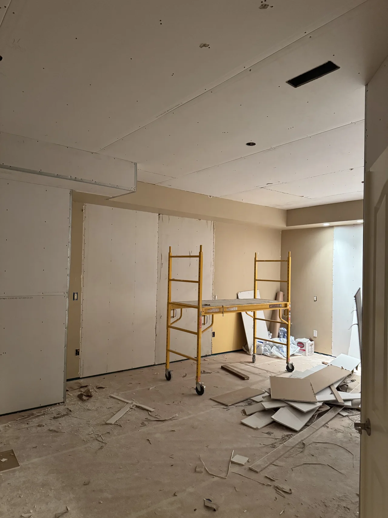 Drywall finishing in an Altus project room, with a scaffold beneath the ceiling.
