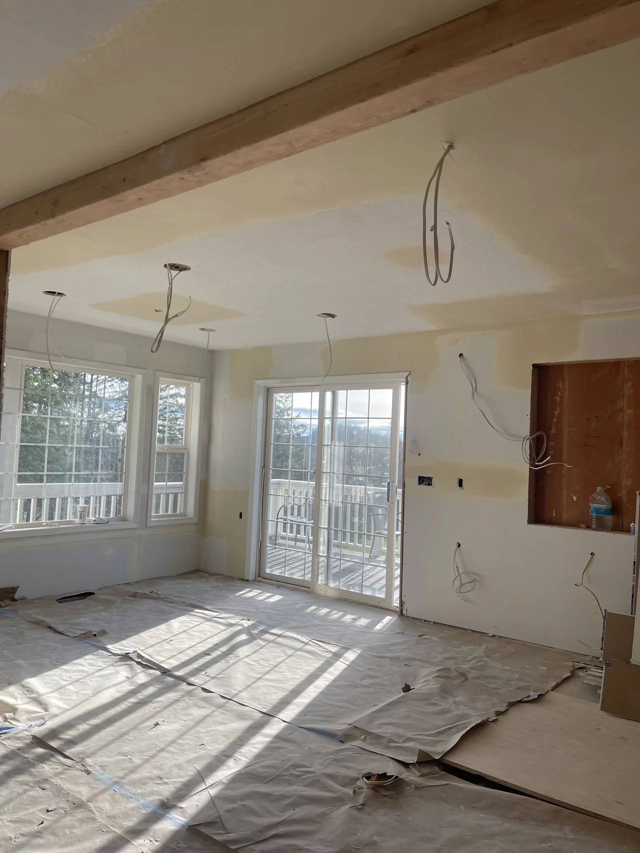 Sunlight falling across taped drywall and protected floors beside a row of windows.