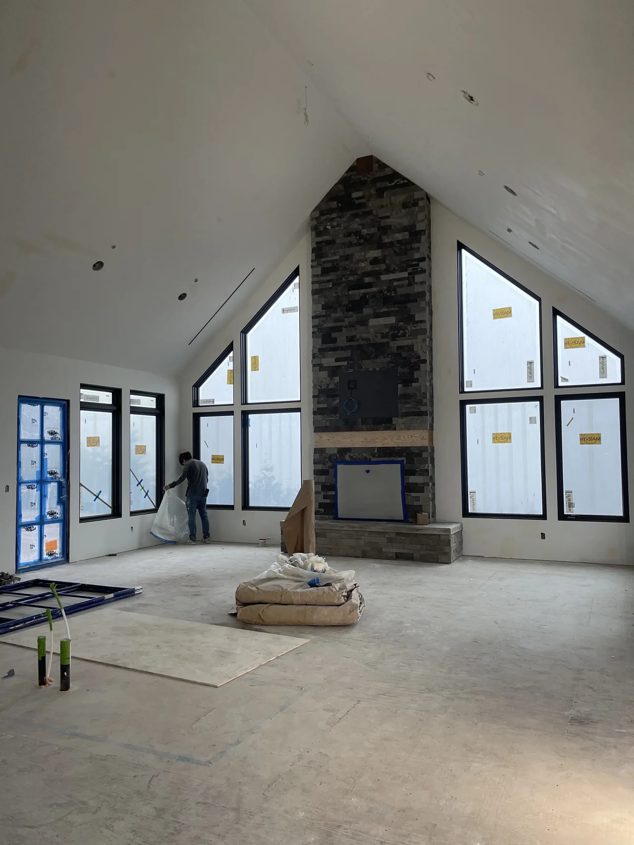 Drywall installation following a vaulted ceiling around tall windows and a stone fireplace.
