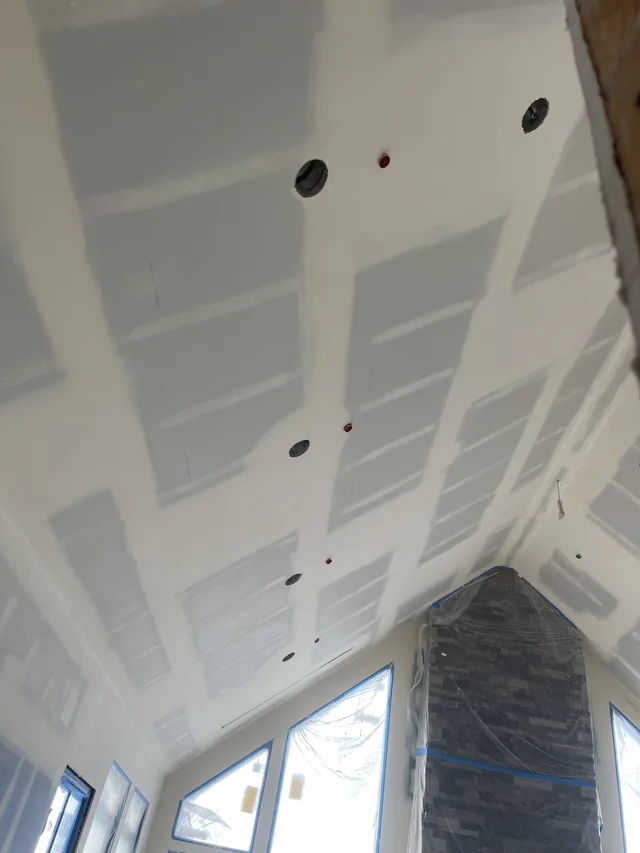 Taped drywall joints on a steep vaulted ceiling beside a stone fireplace.